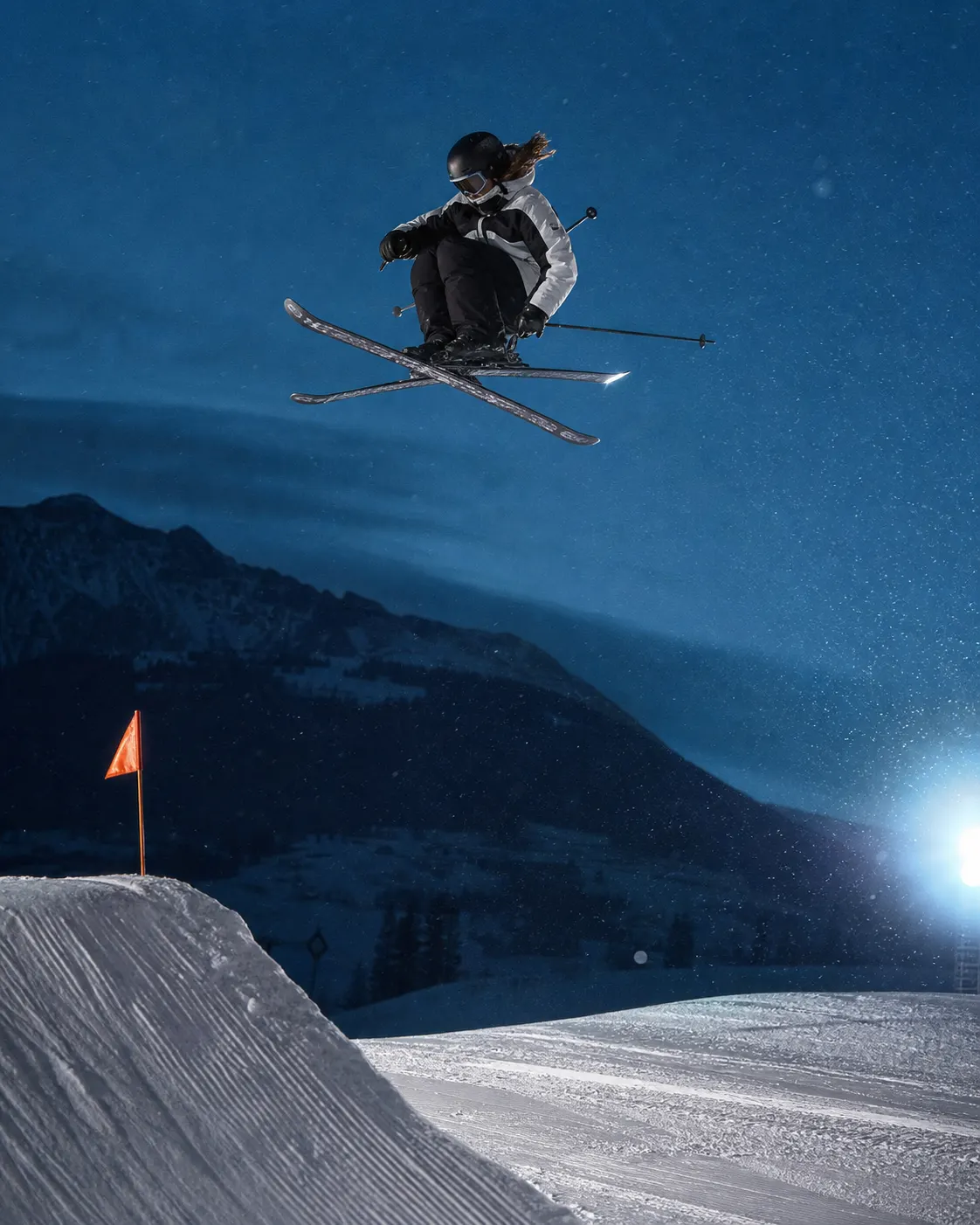 Hana Sato rotates above a snow jump on an illuminated night course.